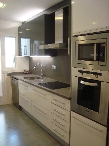 Reforma completa de la cocina con suelos y paredes en porcelánico. Mobiliario lacado en blanco con silestone en encimera y aplacado vertical.